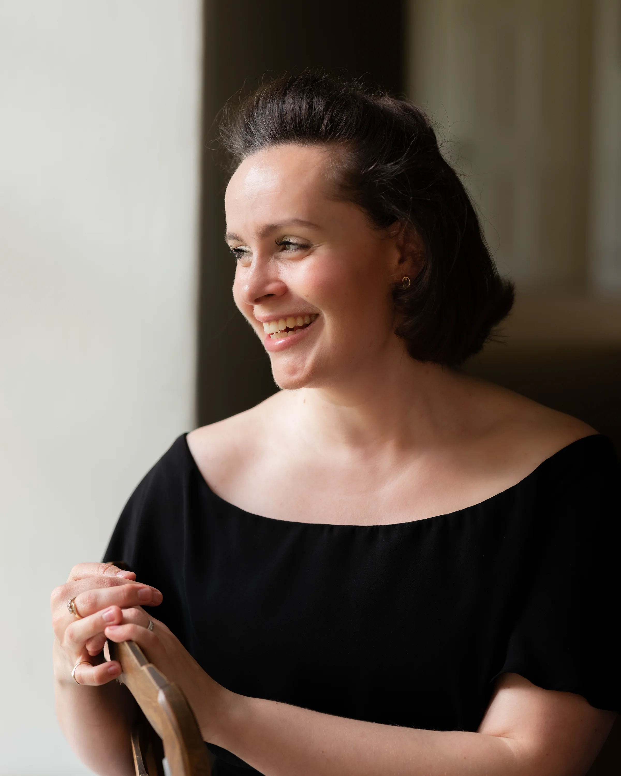 Katy Thomson seated in black, smiling in a softly lit interior